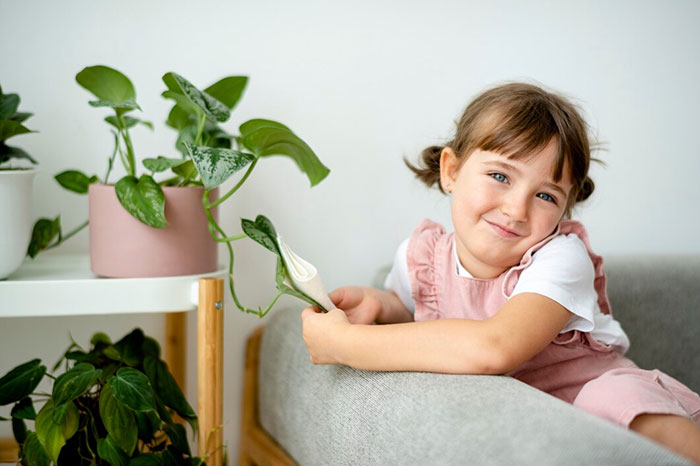 A smiling child with pigtails holding a plant, sitting on a couch, signs of terrible parents not evident.