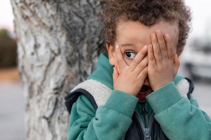 A child in a green hoodie covers their face with hands near a tree, illustrating signs of terrible parents.