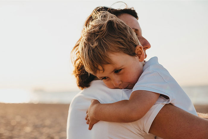 Child embracing a parent on a beach, capturing signs of emotional bonding.