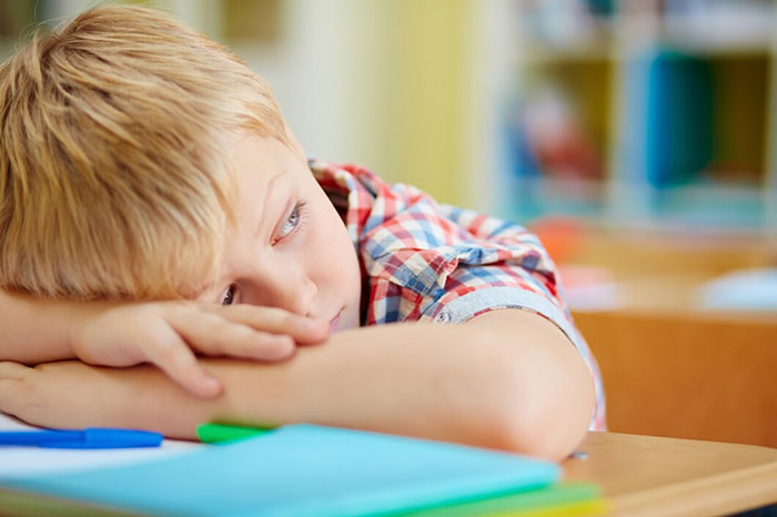 Sad child in classroom, head resting on arms, showing signs of terrible parents.