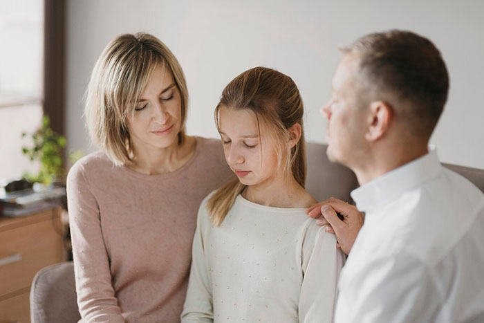 A child looking down with concerned parents, illustrating signs of terrible parenting.