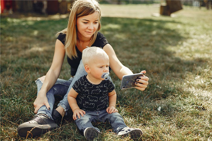 Parent with child sitting on grass, focusing on a smartphone together.