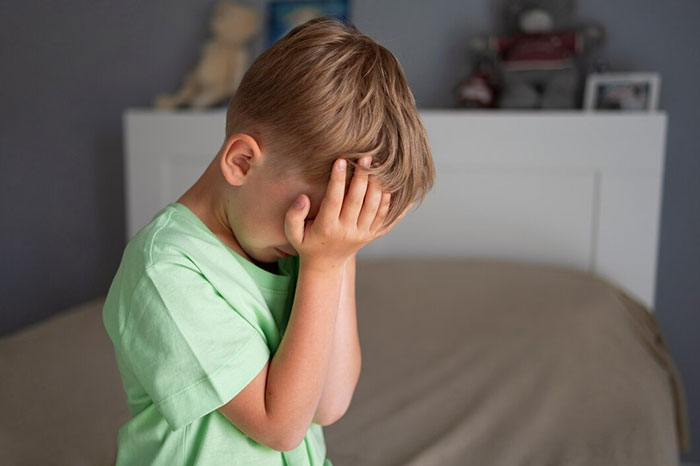 Child in green shirt covering face, expressing distress; represents signs of terrible parents.