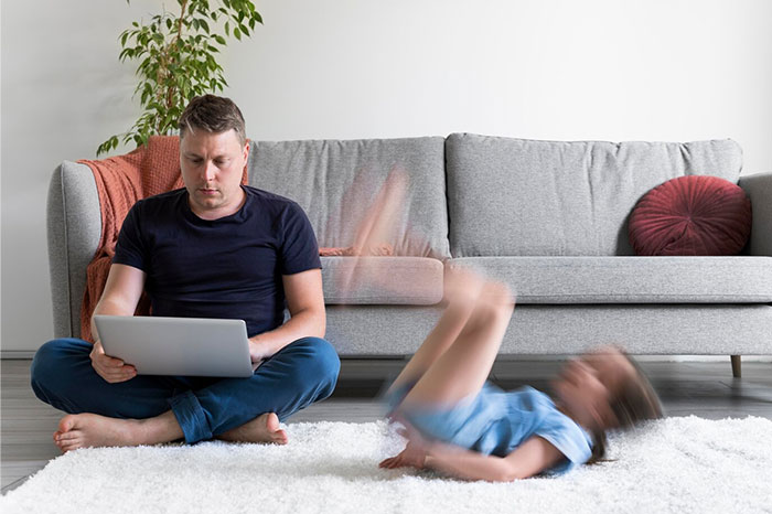 Man engrossed in laptop, ignoring child playing on the floor, illustrating signs of terrible parents.