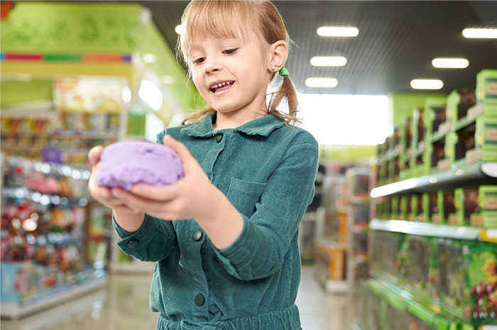 Child smiling and playing with purple clay in a bright toy store, showcasing carefree moments.