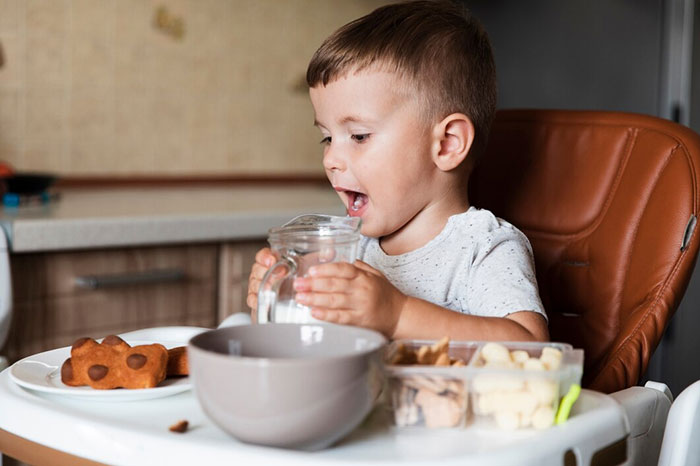 Child sitting in a high chair, drinking from a pitcher, surrounded by snacks, highlighting potential signs of terrible parents.