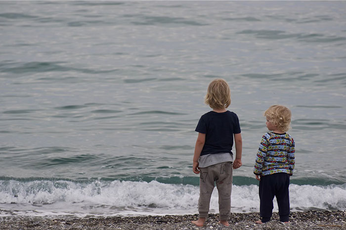 Two children stand alone on a beach, gazing at the ocean.