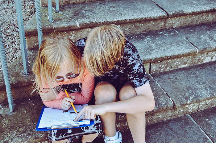 Children sitting on steps, the older one helping the younger with homework, highlighting aspects of parenting.