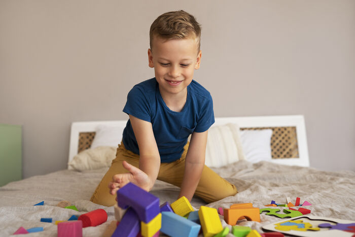 Child playing with colorful blocks on a bed, smiling, in a cozy home setting.