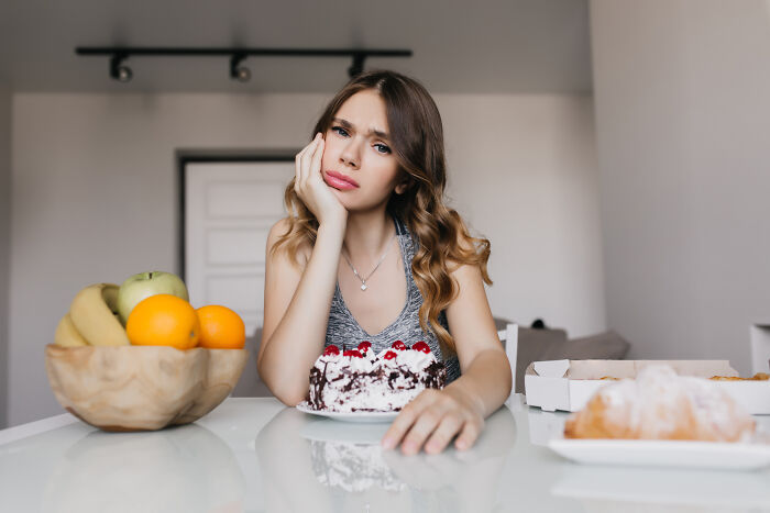 Woman in a kitchen, looking thoughtful, sitting by a cake, symbolizing single-mother-sister-Christmas themes.