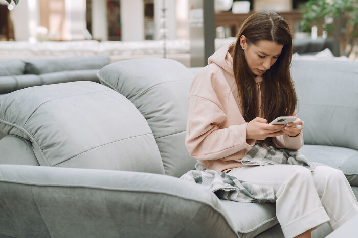 Single mother sitting on a gray sofa, focused on her smartphone, in a cozy living room setting.