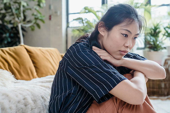 A woman looking pensive, sitting on a couch, reflecting on sibling's boyfriend and Christmas dinner decision.