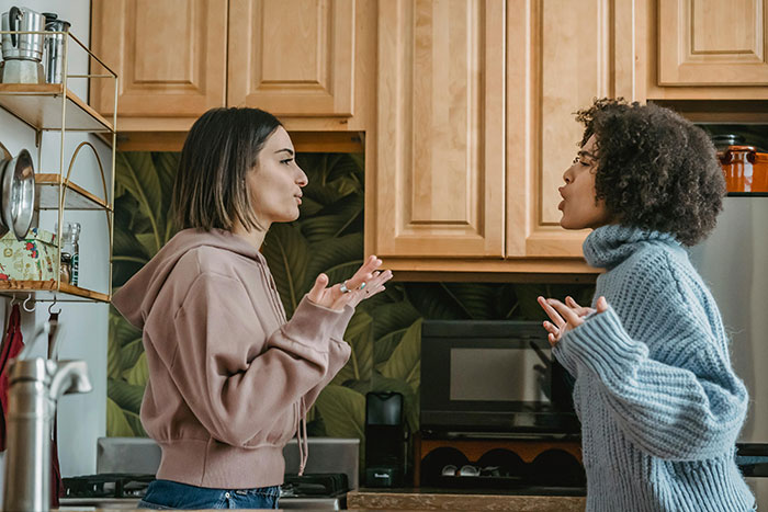 Two sisters arguing in a kitchen, expressing frustration related to a sibling's boyfriend at a holiday dinner.