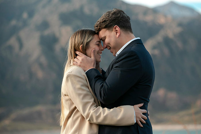 A couple embracing outdoors with mountains in the background.