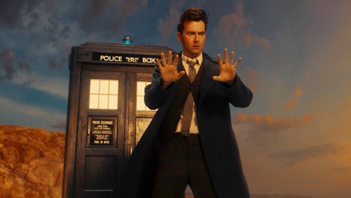 A man in a suit stands in front of a police box, posing dramatically, related to fascinating fan theories.