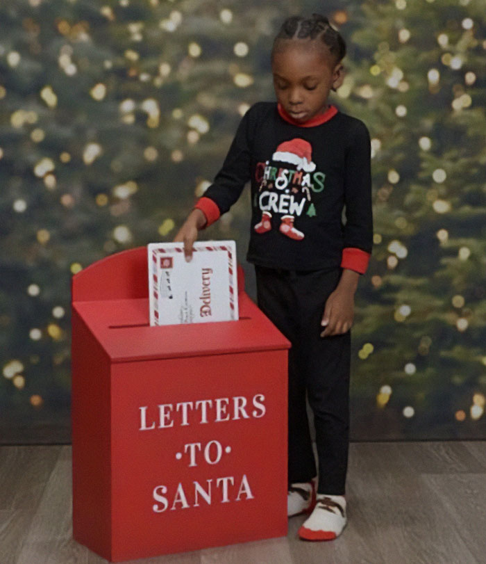 Child in Christmas pajamas at a Letters to Santa box, highlighting the son's unique attire in family photo.