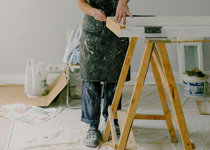 Homeowner working on DIY woodworking project wearing an apron, surrounded by renovation materials.