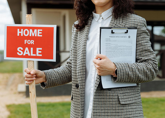 Real estate agent holding "Home for Sale" sign and clipboard, illustrating homeowners dealing with their HOA.