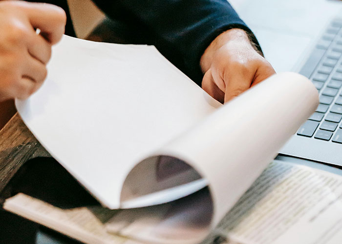 Person flipping through documents beside a laptop, representing homeowners' paperwork on HOA disputes.