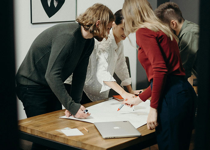 Homeowners discussing strategies around a table, examining blueprints and documents in a collaborative setting.