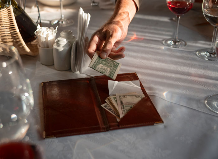 Person placing money in a restaurant bill folder, symbolizing a 50/50 bill split.