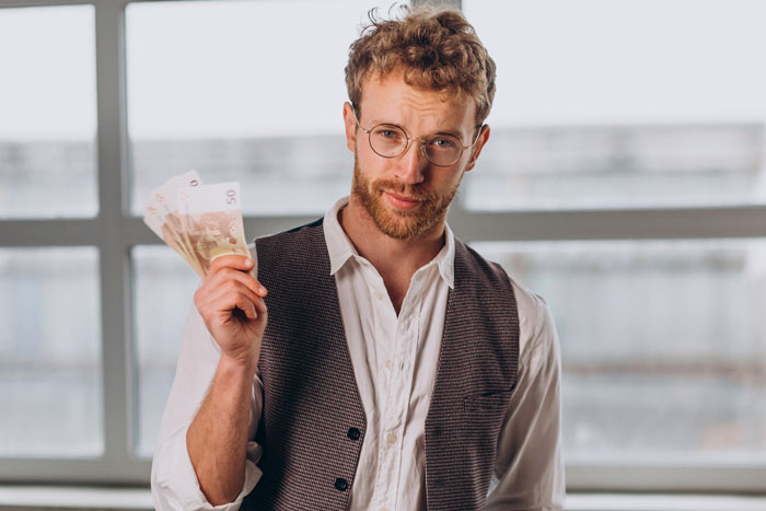 Man with glasses holding 50 euro bills, illustrating the concept of a 50/50 bill split.