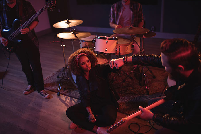 Woman sitting on a music stage with musicians, surrounded by drums and guitars, highlighting a peaceful life transition.