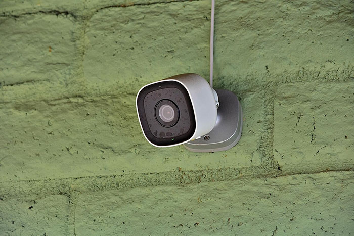 Security camera mounted on a green wall, capturing a peaceful life setting until a stalker reemerges.