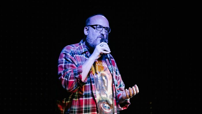 Person in a plaid shirt and glasses holding a microphone, discussing the reality of fun jobs.