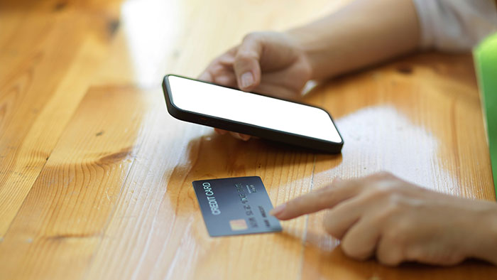 Person holding smartphone and credit card, investigating fraud, focused on financial discrepancy and debt issues.