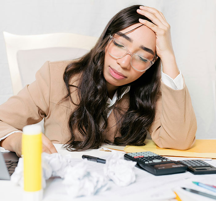 Woman in glasses looking stressed, surrounded by crumpled papers and a calculator, illustrating financial fraud concerns.