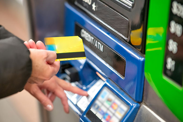 Man inserting a credit card into an ATM, suspecting fraud with debt issues.