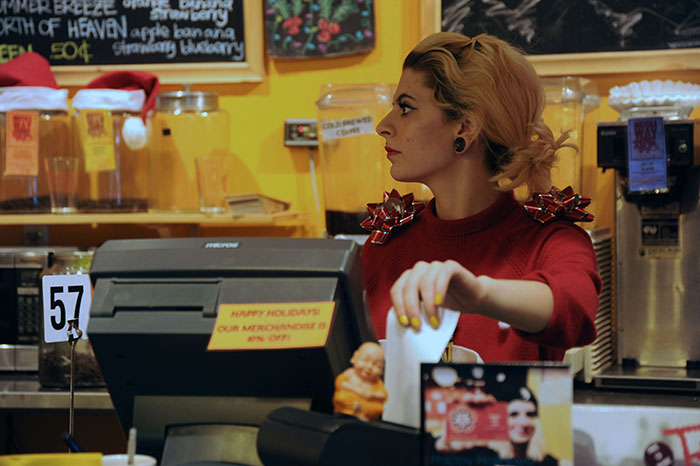 Barista in holiday-themed cafe, surrounded by festive decor, preparing orders.