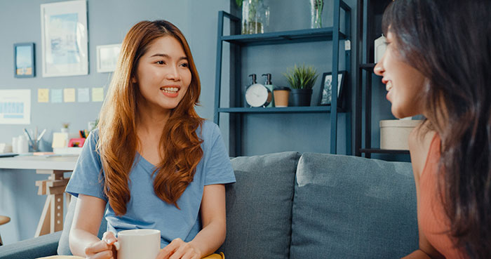 Two women having a conversation on a couch, smiling in a cozy living room.