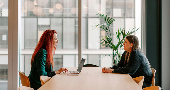 Two women having a conversation in a modern office setting, discussing Canadian language and culture.