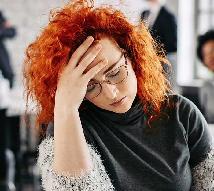 A frustrated woman with red hair and glasses pondering a question, relating to dumb questions about the Canadian language.