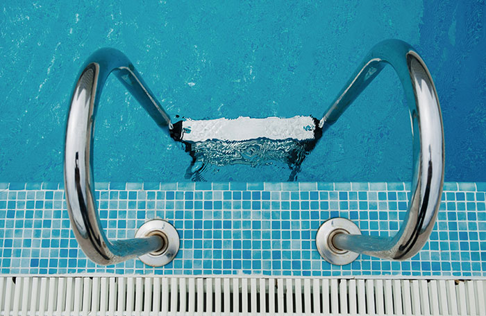 Swimming pool ladder leading into clear blue water, showing the rippling surface.