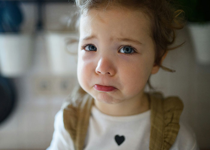 A toddler with a sad expression and blue eyes wearing a white shirt with a heart design, related to dumb police calls.