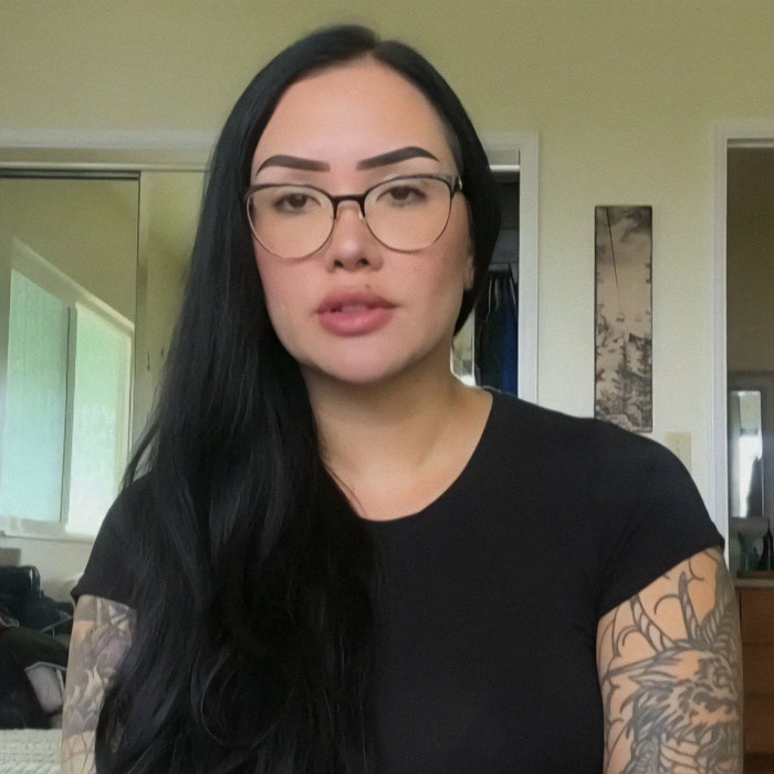 Woman with glasses and tattoos indoors, linked to green card marriage scam case.