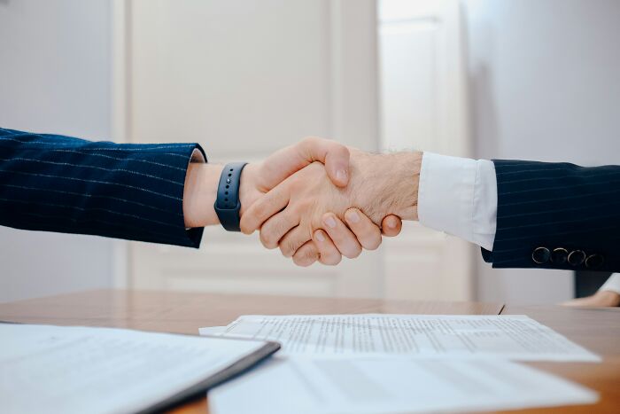 Two people shaking hands over a table with documents, illustrating an astonishing coincidence.