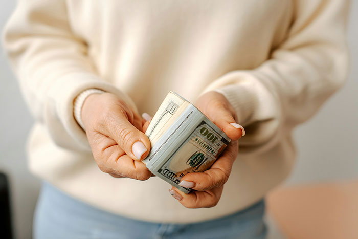 Hands holding a stack of dollar bills, emphasizing a daughter's money.