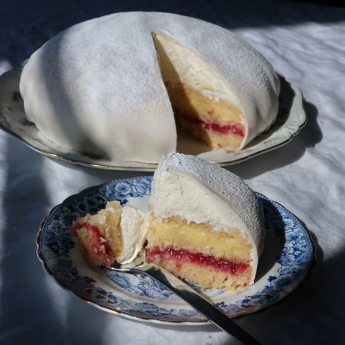 Beautiful food pic of a sliced cake on blue and white plates, featuring creamy layers and raspberry filling.