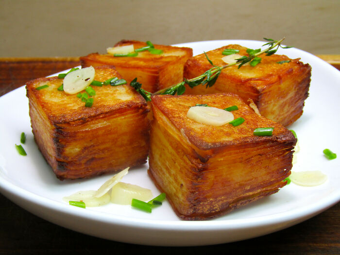 Delicious roasted potato cubes garnished with herbs and garlic on a white plate, a treat for foodies.