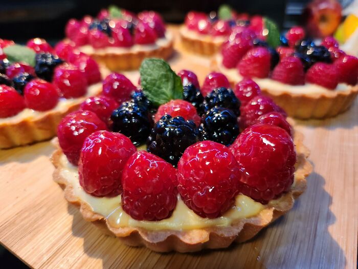 Beautiful food pic of berry tarts with raspberries and blackberries, topped with mint leaves on a wooden board.