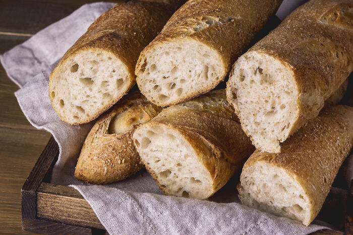 Close-up of fresh baguettes in a wooden tray on a rustic table, showcasing crunchy crust and airy texture.