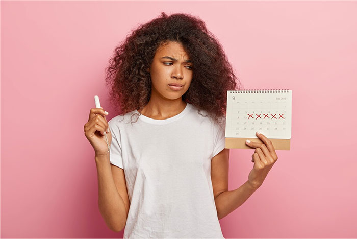 Woman holding a calendar marked with Xs, representing teacher clocking periods, looks puzzled against a pink background.