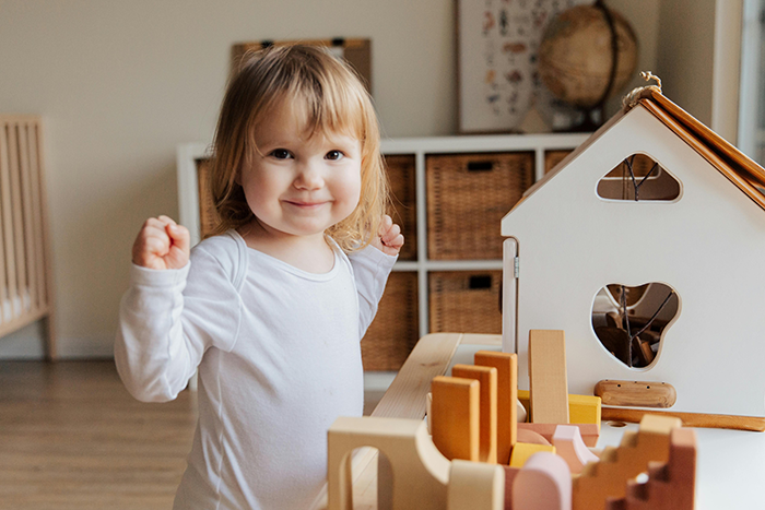 A toddler playing with a wooden toy house set inside a cozy room.