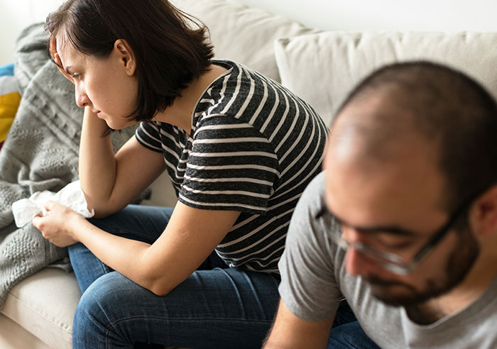 Parents of ten kids looking concerned, sitting on a couch, discussing their eldest moving out.