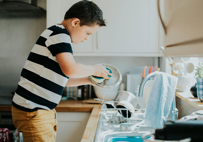 Child washing dishes in a kitchen, wearing a striped shirt, symbolizing family dynamics with 10 kids.