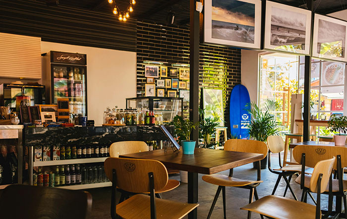 Cozy cafe interior with wooden chairs, small tables, and a surfboard by the window, evoking a trendy and relaxed atmosphere.